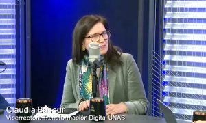 Claudia Bascur, Vicerrectora de Transformación Digital UNAB, sentada en un estudio frente a un micrófono, hablando; fondo con iluminación azul y paneles de vidrio.
